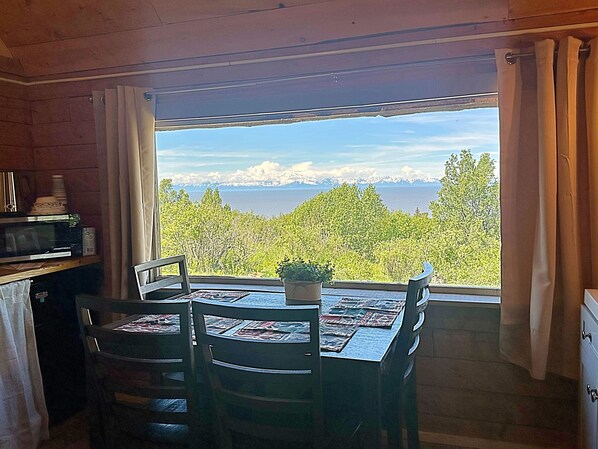 Ein Essbereich mit Tisch und Stühlen, einer Topfpflanze und Blick auf eine gebirgige Landschaft durch ein Fenster.