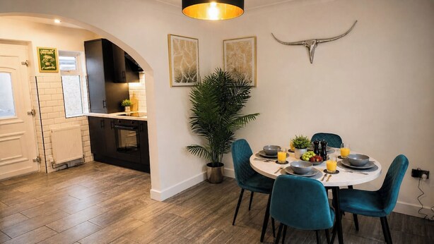 Een moderne keuken met zwarte kastjes, een wit aanrecht en een eethoek met teal stoelen en een witte tafel.