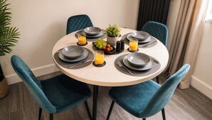 Een ronde eettafel met vier stoelen, elk voorzien van een donkerblauwe kussen. De tafel is gedekt met borden, bestek en een kleine plant in een pot.