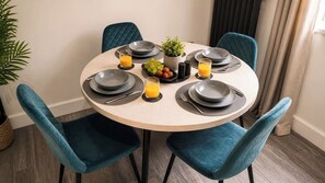 A round dining table with four chairs, each with a dark blue cushion. The table is set with plates, cutlery, and a small potted plant. - Contractor Stays | Close to M18 | Free Parking (Stainforth)