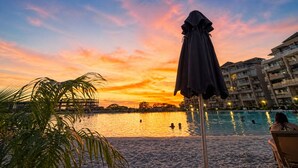 Una playa con piscina, palmeras y un atardecer.