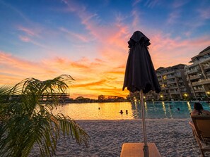 Een strand met een zwembad, palmbomen en een zonsondergang.