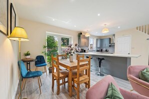 A modern kitchen with a bar stool, a dining table with chairs, and a pink sofa. - Large House, Great for families, Sleeps 5 (Brockworth)