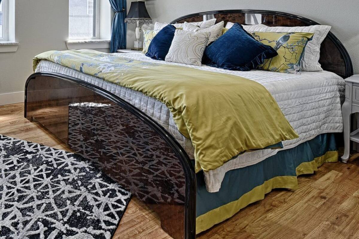 Een slaapkamer met een bed, nachtkastje, lamp en een raam met gordijnen.