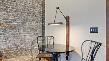 A room with a brick wall, a round table with chairs, a floor lamp, and a power outlet on the wall.