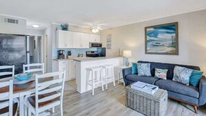 A modern kitchen with white cabinets, a central island, and a dining area with white chairs. - Modern Ocean Oasis - Private Beach • Pool • OceanViews (Hilton Head Island)
