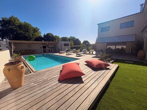 A wooden deck with a pool, red cushions, and a potted plant. - Family villa with pool & summer kitchen  (Beaupuy)