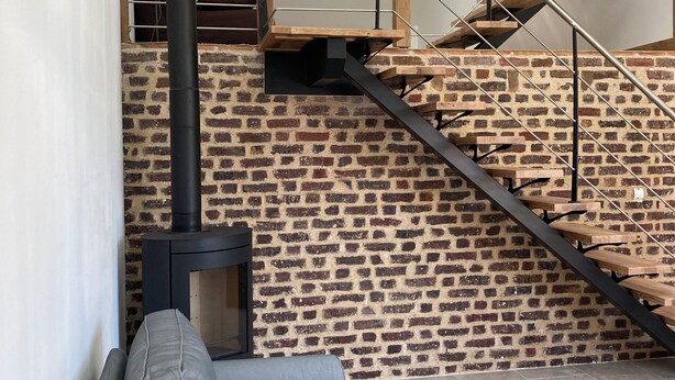 A modern living space with a brick wall, a sofa, a table, and a staircase with a metal railing. - The swallow barn (Azé)