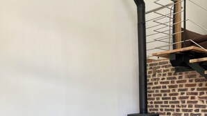 A gray sofa, a wooden table, and a wood-burning stove against a brick wall. - The swallow barn (Azé)