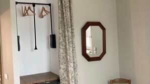 A room with a wooden chair, a hanging light fixture, a mirror, and a shelf with a hanging rack. - The swallow barn (Azé)