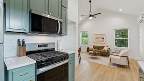 Una cucina con piano cottura a gas, forno a microonde e mobili verdi. C'è una zona pranzo con divano e ventilatore a soffitto.