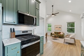 Une cuisine équipée d’une cuisinière à gaz, d’un four à micro-ondes et de meubles de couleur verte. On y trouve également un coin repas avec un canapé et un ventilateur de plafond.
