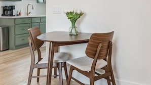 Un'area pranzo con un tavolo rotondo e quattro sedie, un vaso con fiori e una cucina sullo sfondo.