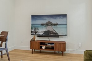Un téléviseur à écran plat fixé au mur, au-dessus d’un meuble de rangement en bois, avec une image d’un paysage marin tropical.