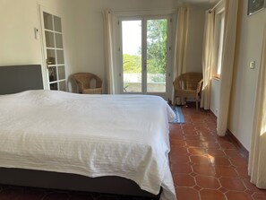 Ein Schlafzimmer mit einem großen Bett, einem Kleiderschrank, einem Balkon mit Sitzgelegenheiten und Blick auf Grünflächen.