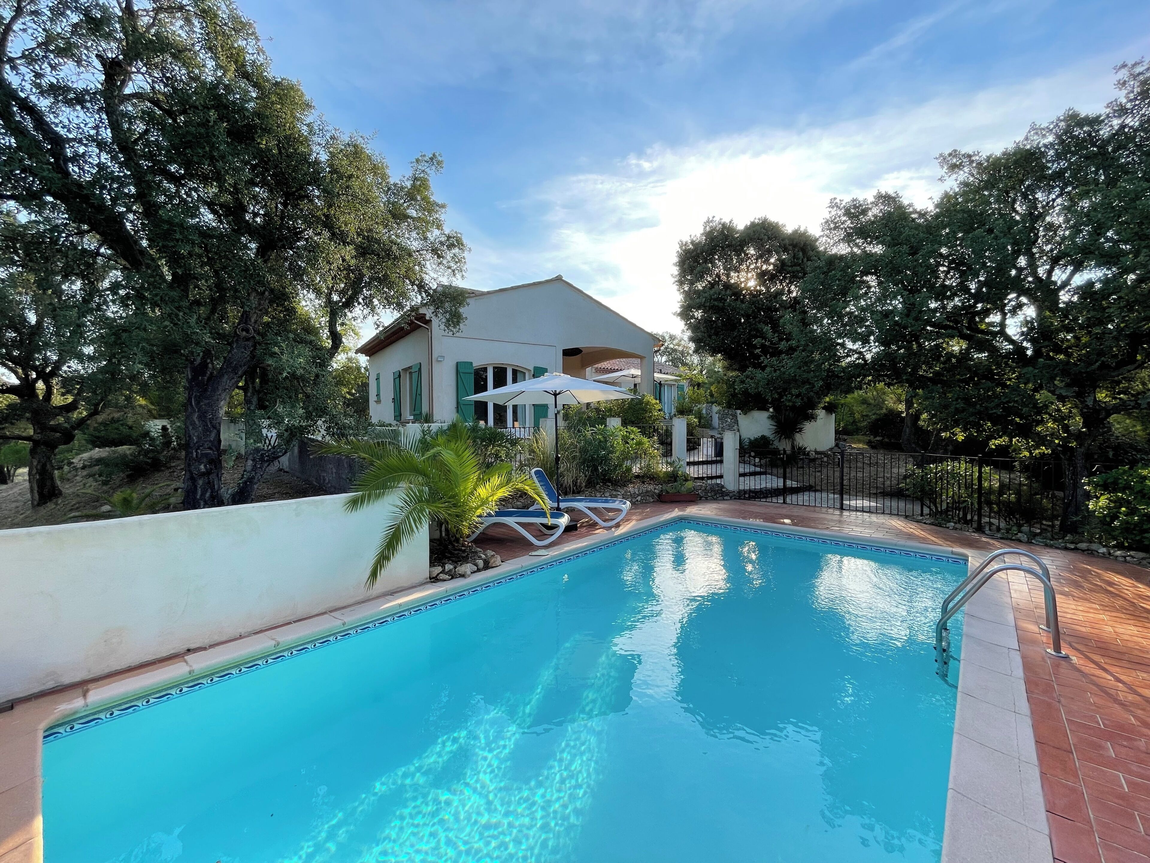 A swimming pool with lounge chairs, a house with a balcony, and surrounding trees.