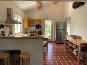 Eine moderne Küche mit Holzausstattung, Edelstahlgeräten, einer großen Kochinsel mit Sitzgelegenheiten und einem Fliesenboden.