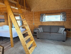 Ein Holzhütten-Innenraum mit einem Doppelstockbett, einer Couch und einer Leiter.