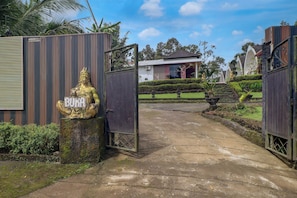 Une entrée fermée par un portail orné d’une statue, un chemin menant à un bâtiment et des jardins bien entretenus.