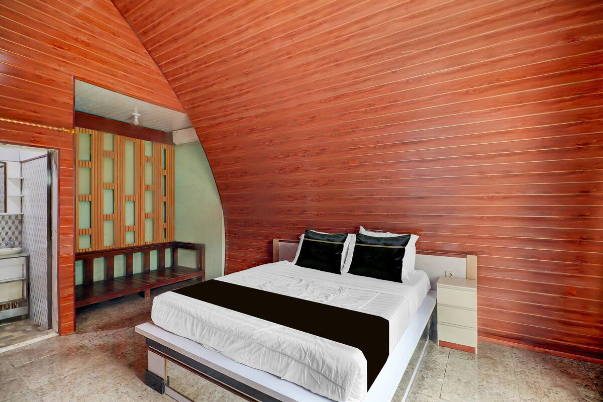 Ein Schlafzimmer mit schräg angesetzter Decke, einem Bett mit weißer Bettwäsche, einem Nachttisch und einer Bank.