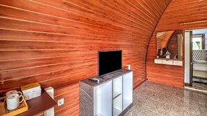 A room with a wooden ceiling, a flat-screen TV on a cabinet, a coffee table with mugs, and a mirror.