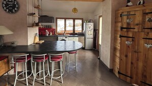 A kitchen with a central island, bar stools, a refrigerator, and a clock. - Cosy village house (Jausiers)