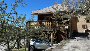 A building with a wooden balcony, a car parked in front, and a gravel driveway. - Cosy village house (Jausiers)
