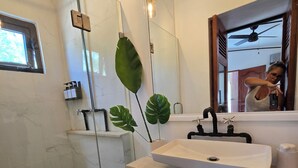Un bany modern amb una cabina de bany de vidre, un lavabo blanc i un mirall gran.