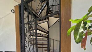 Una escala espiraltra amb barana metàl·lica que condueix a un pis superior, una cadira de vimet i una planta en test.