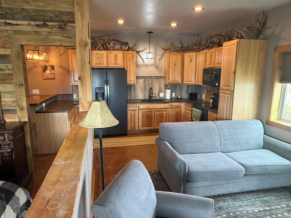 A modern kitchen with wooden cabinets, a refrigerator, and a dining area with a grey sofa.
