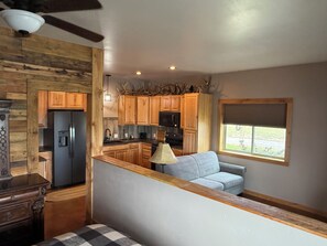 A kitchen with wooden cabinets, a refrigerator, a microwave, and a dining area with a table and a couch.