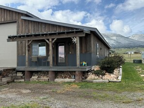 A rustic cabin with a porch, stone foundation, and a view of mountains.