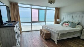 Ein Schlafzimmer mit Bett, Schreibtisch, Stuhl, Fenster mit Meerblick und Deckenleuchte.