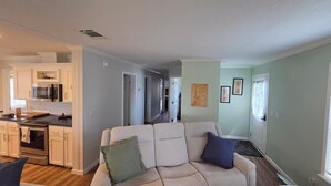 Ein Wohnzimmer mit einer Couch, eine Küche mit weißen Schränken und ein Flur, der zu Schlafzimmern führt.