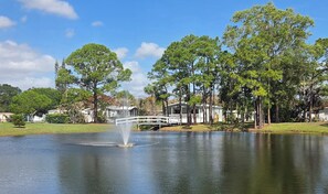 A lake with a fountain, surrounded by trees and a white bridge. - Your Stuart Oasis (Stuart)