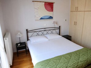 Ein Schlafzimmer mit Bett, Nachttisch, Lampe, Heizkörper und Kleiderschrank.