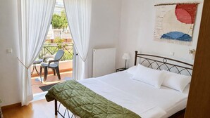 A bedroom with a bed, a green bedspread, white curtains, a chair, and a painting on the wall. - Pavlos Apartment - Leontari Stay with Garden View (Leontario)