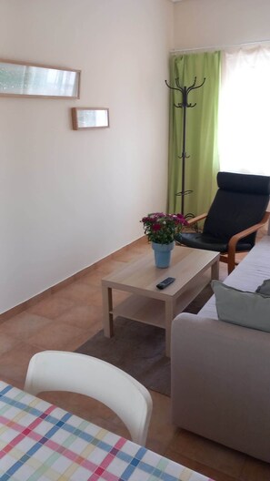 Un salon comprenant un canapé, une petite table avec un vase de fleurs, un fauteuil et un porte-manteau.