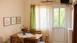 A dining area with a table, chairs, a vase with flowers, and a window with curtains. - Pavlos Apartment - Leontari Stay with Garden View (Leontario)