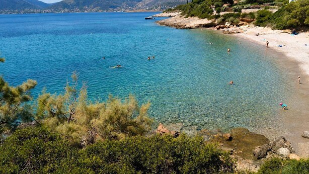 Una spiaggia costiera con acque blu cristalline, un litorale roccioso e vegetazione.