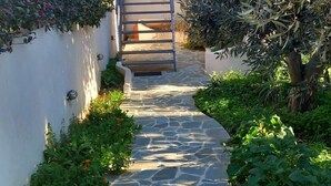 Un vialetto in pietra conduce all'ingresso di un edificio, circondato da vegetazione e un muro bianco.