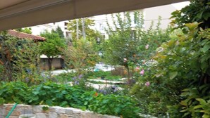 Un'area patio esterna con pareti in pietra, un'area salotto coperta con sedie e un giardino ricco di piante e fiori.