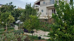 Un edificio a due piani con un balcone, immerso nel verde e circondato da un giardino.
