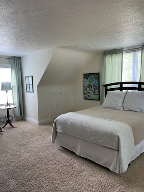 Un dormitorio con cama, una ventana con cortinas, un cuadro en la pared y una lámpara sobre una mesa.