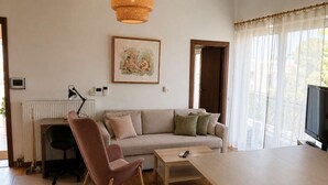 Una sala de estar con sofá, sillón, mesa de centro, televisor y ventana con cortinas.