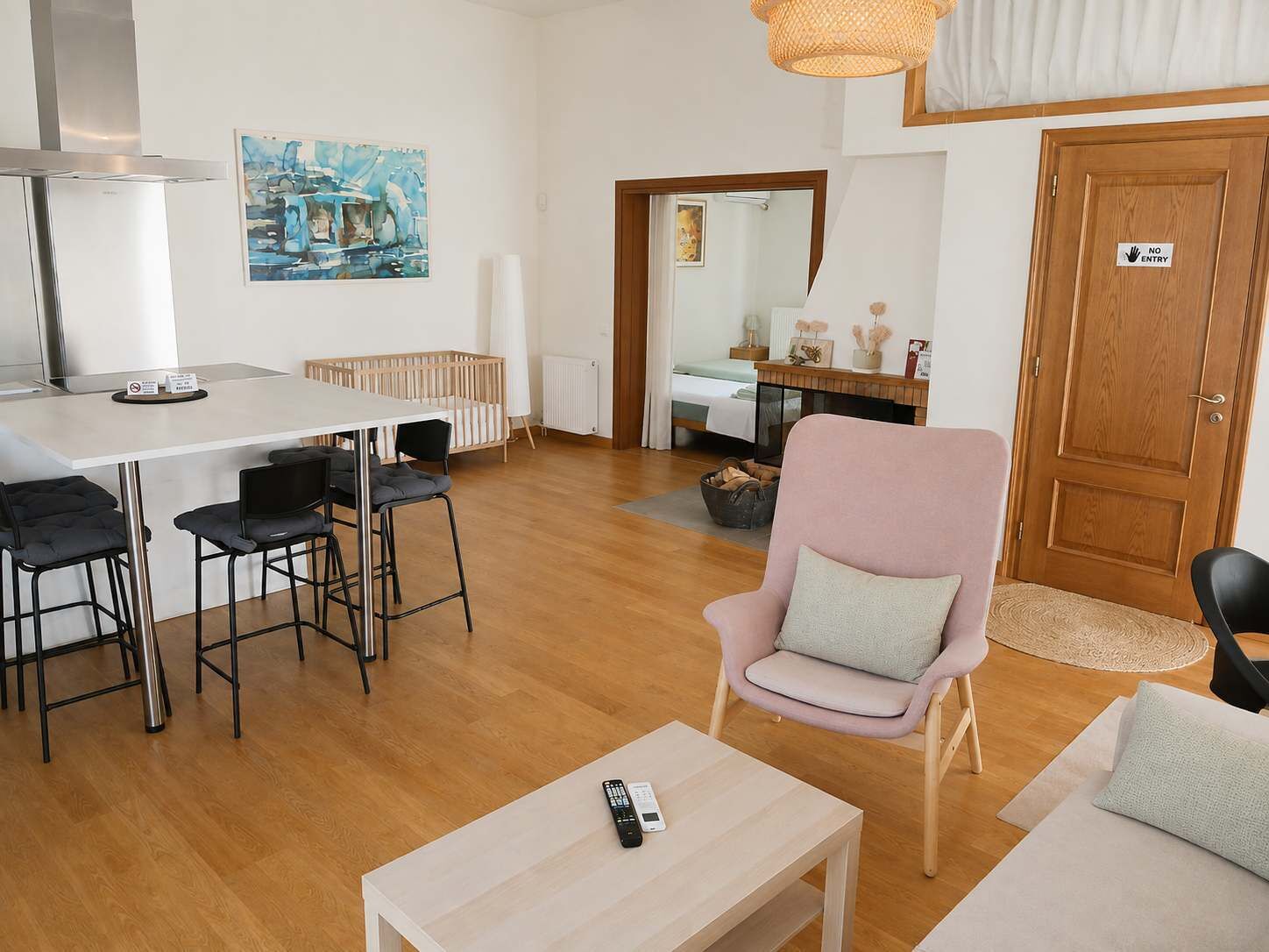 A modern living room with a dining area, a wooden floor, a white sofa, a pink armchair, and a kitchen area with a refrigerator.