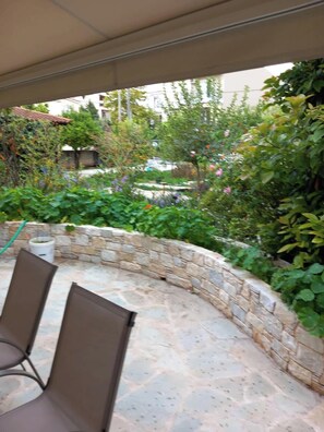 An outdoor patio area with stone walls, a covered seating area with chairs, and a garden with various plants and flowers. - Pavlos Loft - Garden Views & Terrace in Leontari (Leontario)
