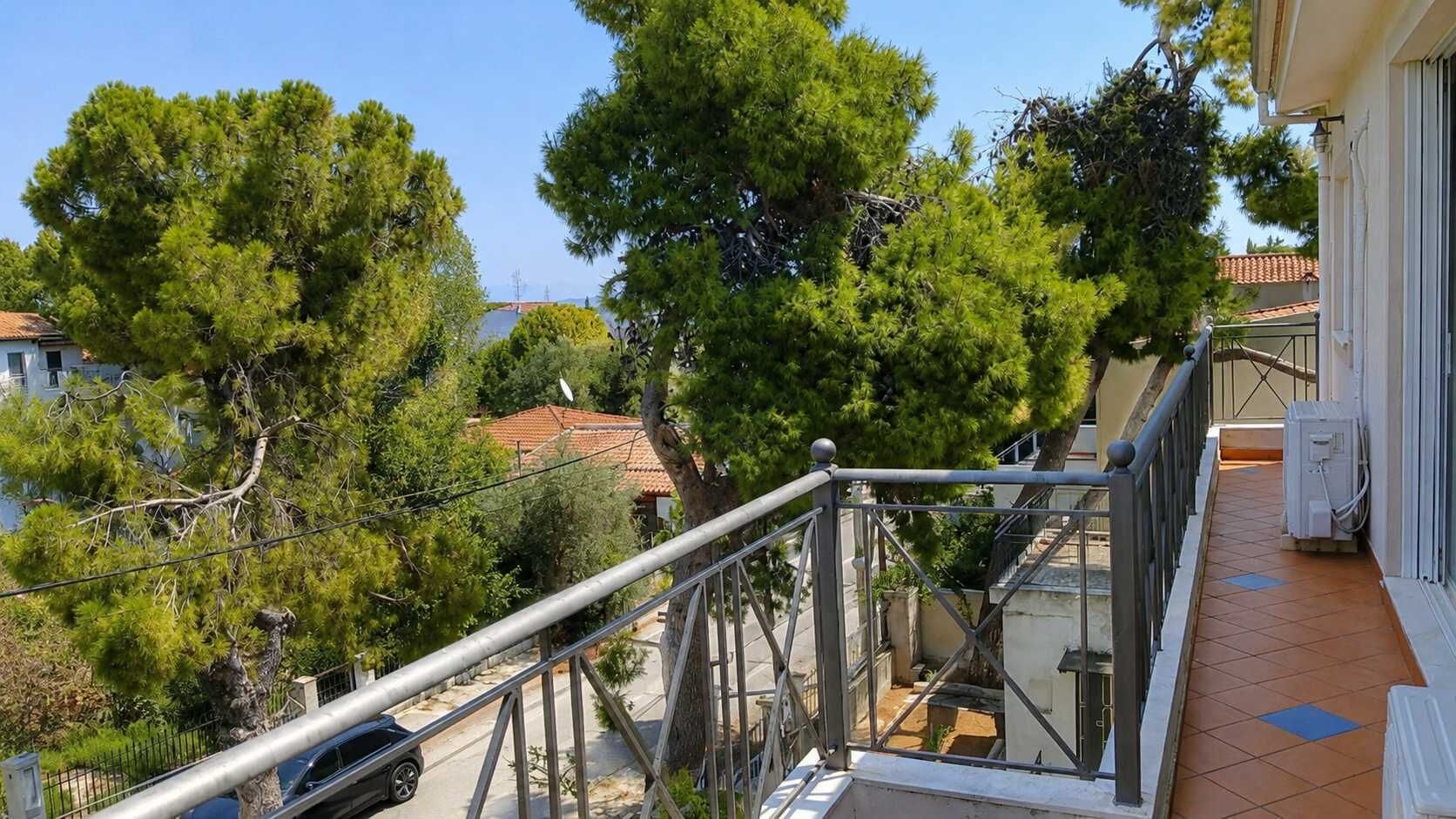 Un balcon doté d’une rambarde en métal, donnant sur un quartier résidentiel avec des arbres et des maisons.