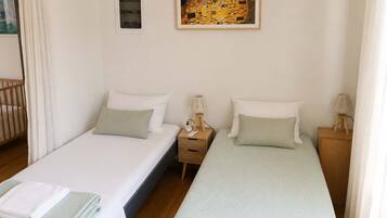 Une chambre d’hôtel avec deux lits simples, une table de chevet avec une lampe, un tableau au mur et une fenêtre avec des rideaux.