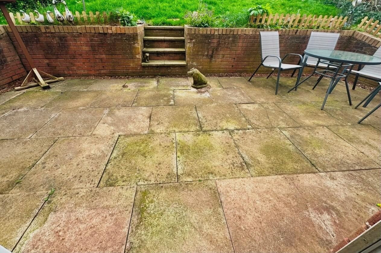 Un espace extérieur aménagé en patio, avec un sol en pierre, un mur en briques, un escalier et une table entourée de chaises.